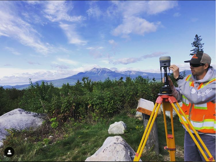 photo of an engineer using surveying equipment on a mountain with a mountain in the background