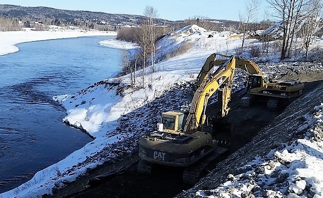 photo of excavators working on a dirt road alongside a river in winter