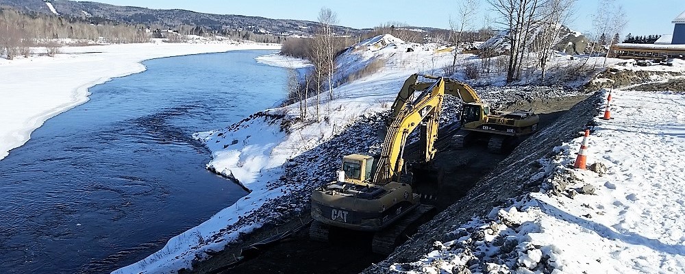 photo of excavators working on a dirt road alongside a river in winter