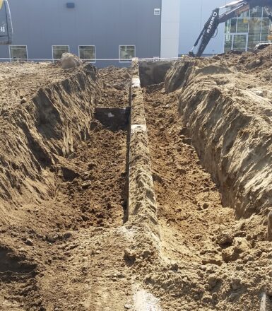 exterior photo of excavation equipment filling in a ditch at a construction site