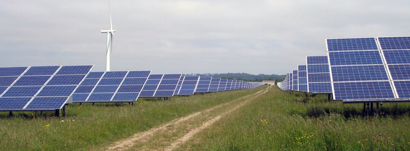 Field of solar panels with a wind turbine in the background.