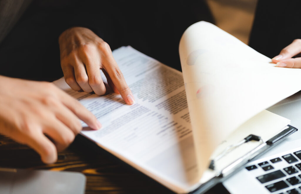 Image of two people in an office setting pointing at a document on a clipboard atop a laptop.